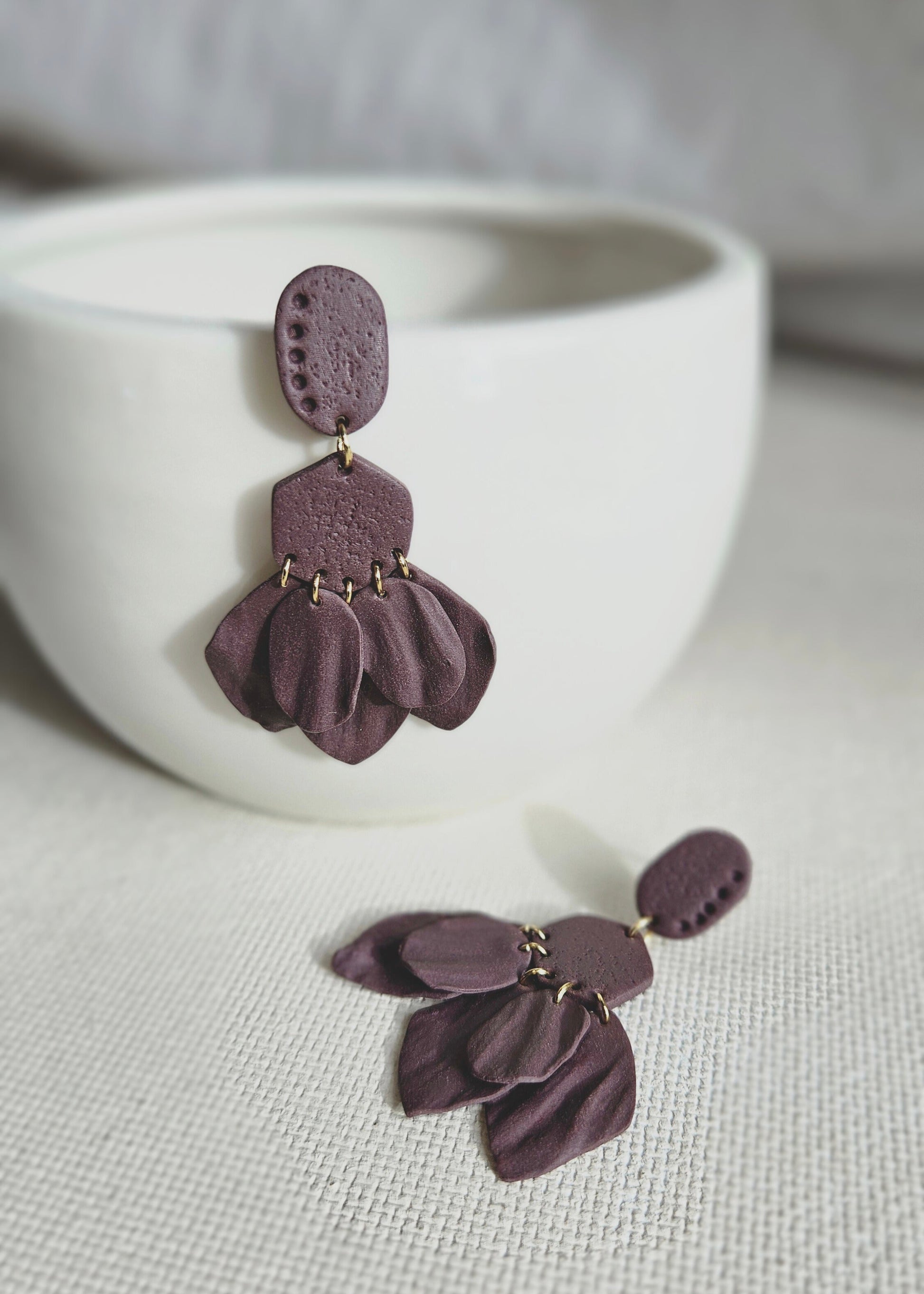 La paire de boucles d'oreilles Pétillante dans son coloris Violet foncé est présentée à plat, devant un rideau