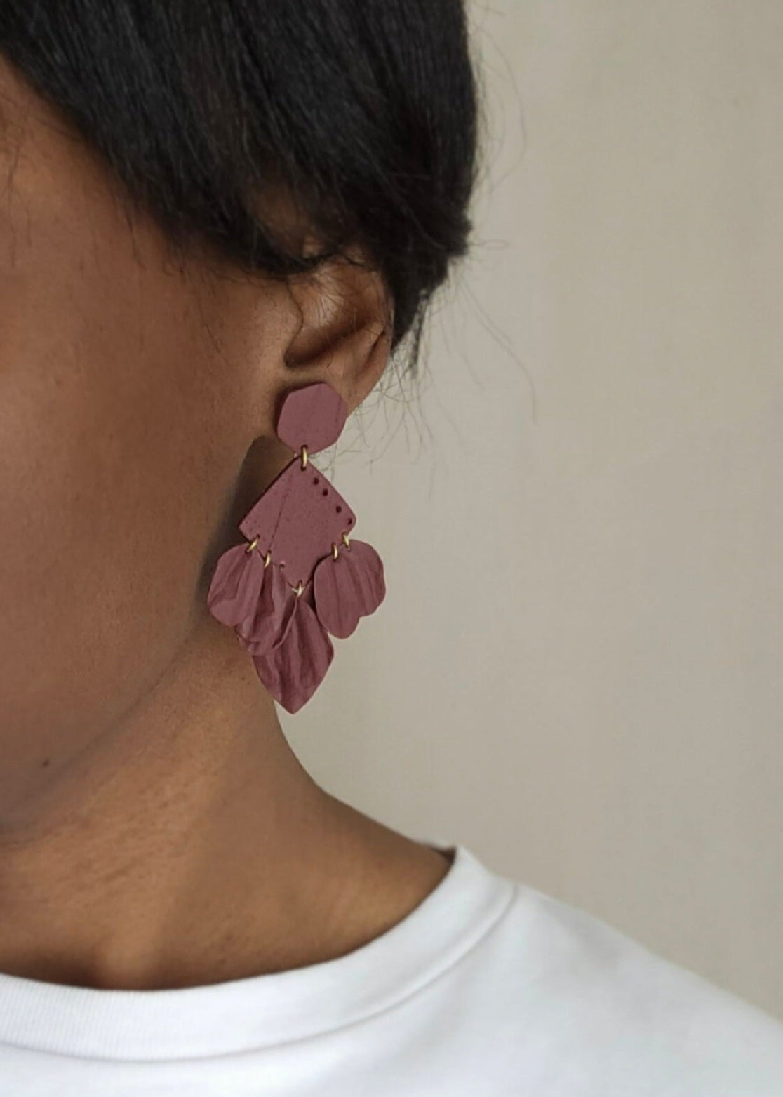 Le mannequin porte la paire de boucles d'oreilles Épanouie dans son coloris Bordeaux. Ce modèle est composé de feuilles légères qui forment un bouquet