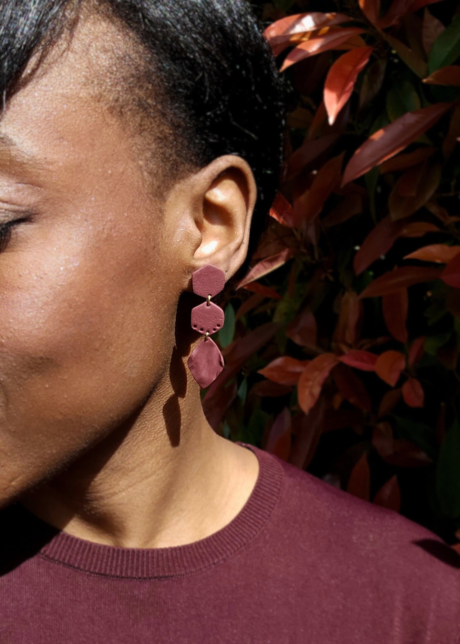 Le mannequin porte la paire de boucles d'oreilles Naturelle dans son coloris Bordeaux. Ce modèle est composé d'une feuille légère