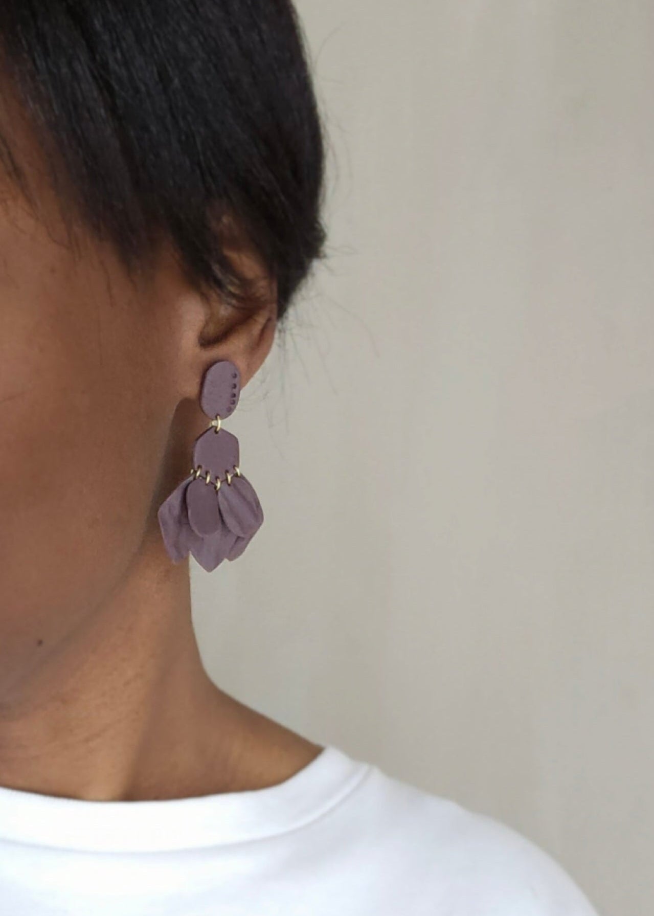 Le mannequin porte la paire de boucles d'oreilles Pétillante dans son coloris Violet foncé. Ce modèle est composé de feuilles légères qui forment un bouquet