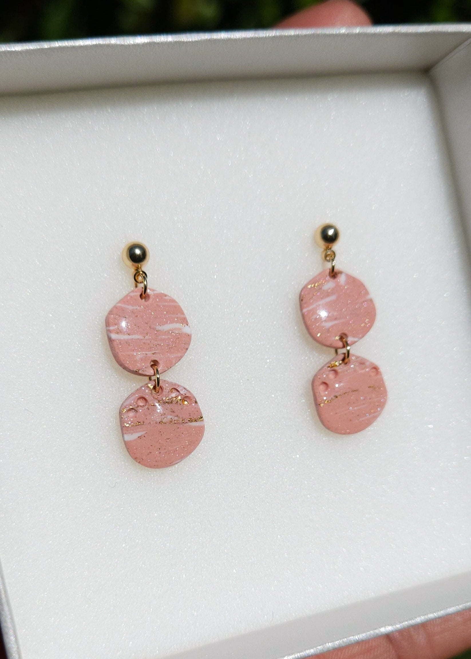 La paire de boucles d'oreilles Intuitive dans son coloris Douceur poudrée est présentée à plat, dans son écrin blanc